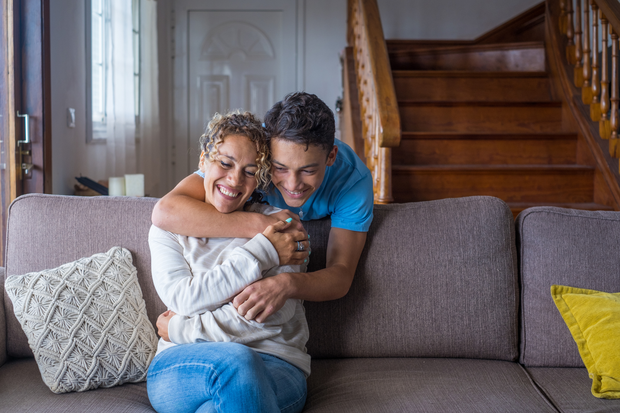 Happy middle age mother spend time with teenager son, relatives people hugging at home, adult attentive millennial grateful child wrapped in a plaid or warm sweater loving mommy caring about her comfort