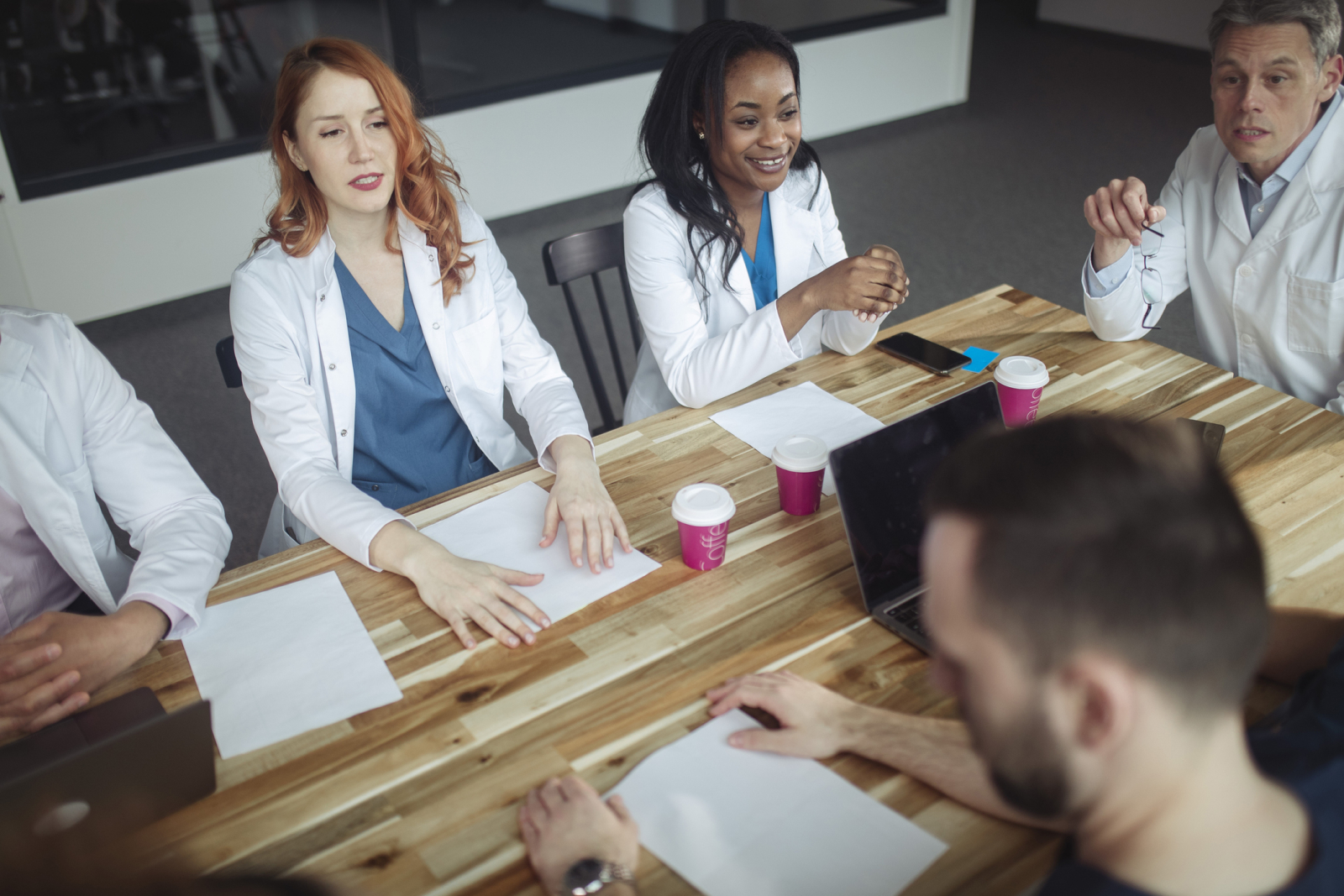 Group of five medical professionals sitting at a table in a supportive debrief meeting