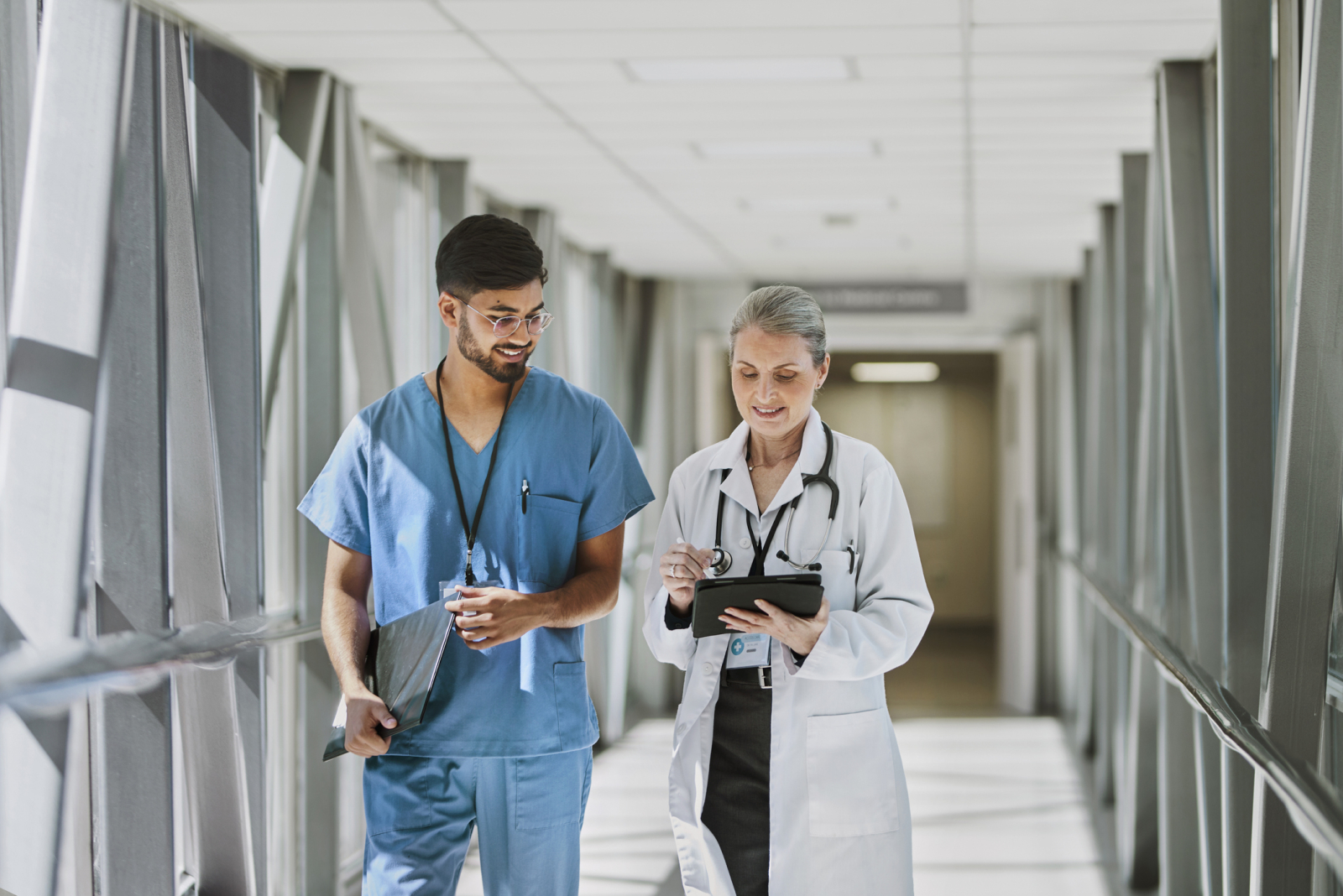 Female doctor holding digital tablet and nurse walking together in corridor, smiling and discussing work